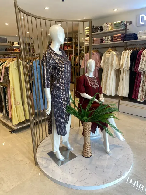 Mannequins on a round marble plinth framed by a curved brass-finish screen