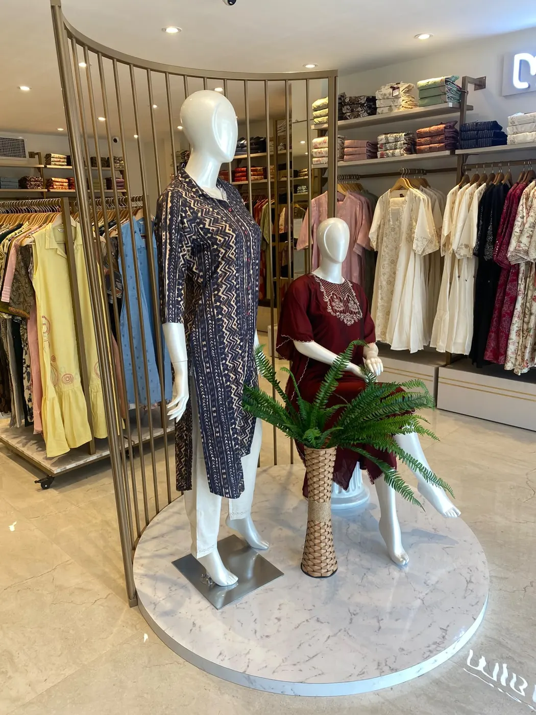 Mannequins on a round marble plinth framed by a curved brass-finish screen